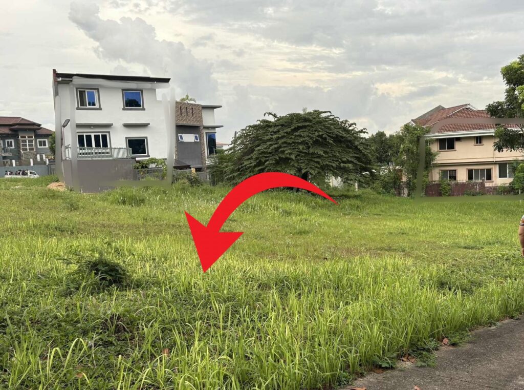 A red arrow pointing to a large, empty green lot in front of a white house in a subdivision.