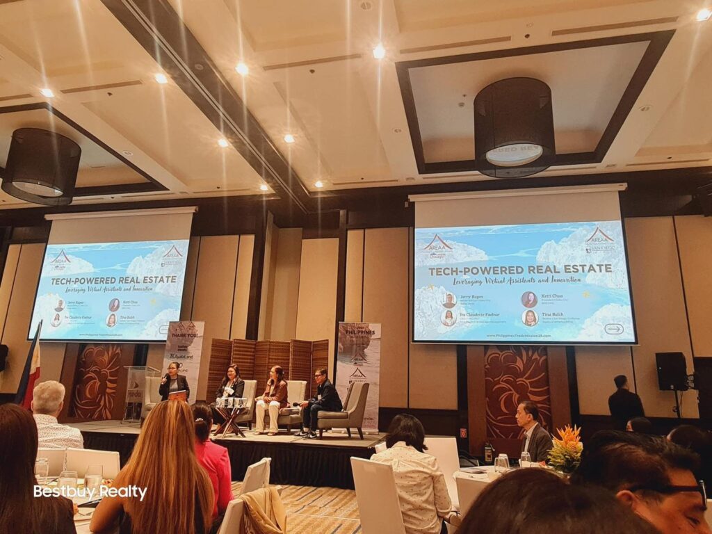 A panel discussion on a stage about "Tech-Powered Real Estate" featuring speakers Ire Claudette Faelnar, Jerry Bayon, and Tina Balch.