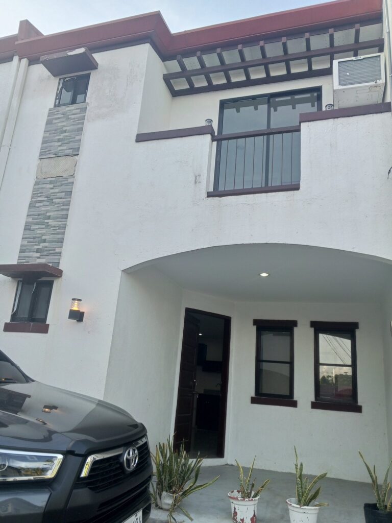 Front exterior view of the 2-storey townhouse in Consolacion with a "FOR SALE" sign and modern grey/white finish.