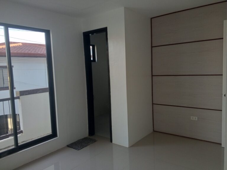A spacious bedroom with a large window and a white door leading into the private en suite bathroom.